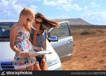 Two young women with car look at road map with mountain landscape in background