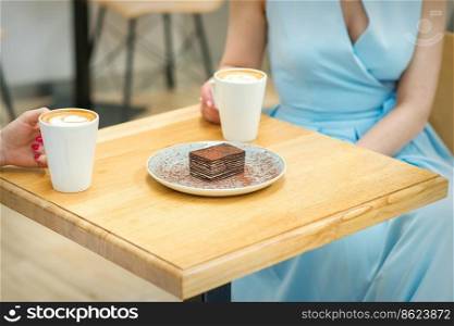 Two young women with cups of coffee and pieces of cake sitting at the table in a cafe outdoors. Two women with sitting at the table in cafe