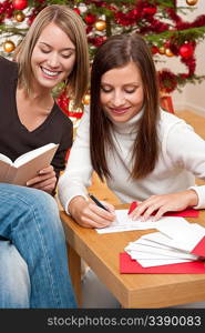 Two young women writing Christmas cards in front of tree