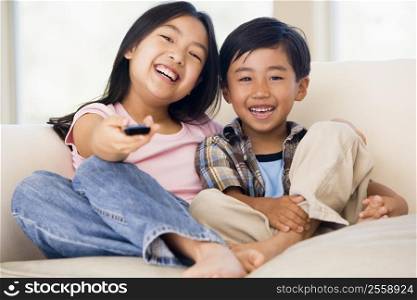 Two youngchildren in living room with remote control smiling