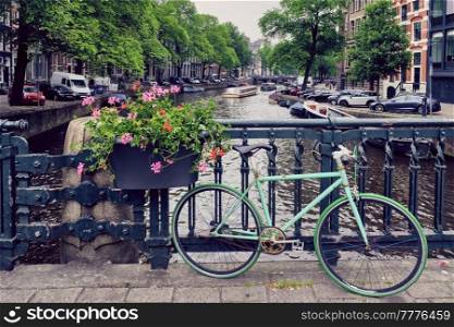 Typical Amsterdam view - Amsterdam canal with boats and parked bicycles on a bridge with flowers. Amsterdam, Netherlands. Amsterdam canal with boats and bicycles on a bridge