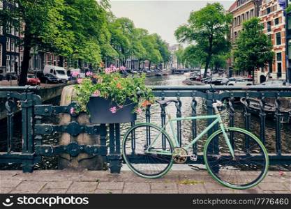 Typical Amsterdam view - Amsterdam canal with boats and parked bicycles on a bridge with flowers. Amsterdam, Netherlands. Amsterdam canal with boats and bicycles on a bridge