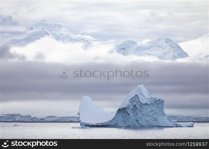 Typical Antarctica, large iceberg swims through the calm sea in front of a cloud wall