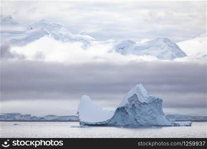 Typical Antarctica, large iceberg swims through the calm sea in front of a cloud wall