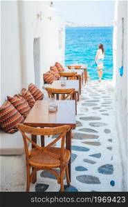 Typical Greek bar in Mykonos town with sea view, Cyclades islands, Greece. Benches with pillows in a typical greek outdoor cafe in Mykonos with amazing sea view on Cyclades islands