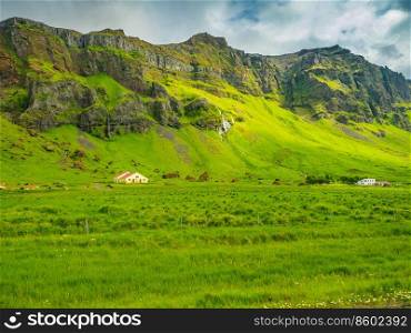 Typical icelandic summer landscape with mountain, waterfalls, green field, cows and barn