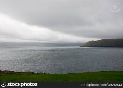 Typical landscape on the Faroe Islands as seen from Kirkjubour with green grass, mountains and sea