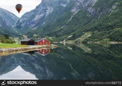 typical norway fjord with red wooden houses and reflection in the water and hot air balloon in the sky