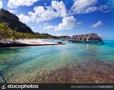 Typical Polynesian landscape - seacoast with palm trees and small houses on water.