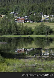 typical red and white houses in norway with reflection in the water of the leira fjord in middle norway