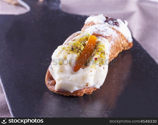 Typical sicilian cannolo, lying over black stone background