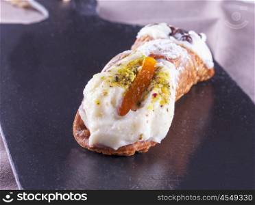Typical sicilian cannolo, lying over black stone background