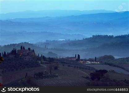 typical Tuscan landscape - a view of a villa on a hill, a cypress alley and a valley with vineyards, province of Siena. Tuscany, Italy