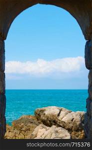 Tyrrhenian sea and rocky coast through arch in Cefalu, Sicily, Italy