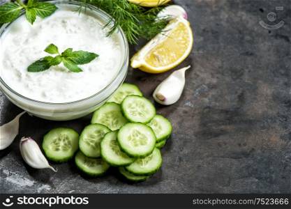 Tzatziki sauce with ingredients cucumber, garlic, dill, lemon, mint on grungy background. Healthy food