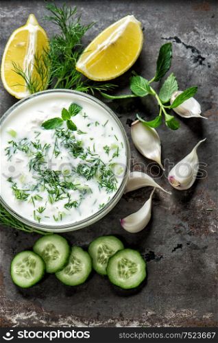 Tzatziki sauce with ingredients vegetables and herbs on grungy background