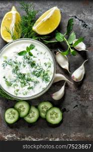 Tzatziki sauce with ingredients vegetables and herbs on grungy background
