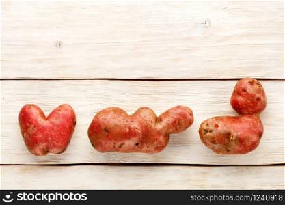 Ugly funny vegetables, heart-shaped potatoes and letter shape on a white wooden background, close-up. Top view, copy space.. Ugly funny potato in the heart shape and letter shape on a white wooden background. Vegetables or food waste concept. Top view, close-up.