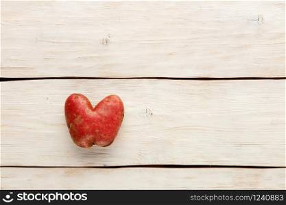 Ugly funny vegetables, heart-shaped potatoes on a white wooden background. The concept of grungy vegetables or food waste. Top view, copy space.. Ugly potato in the heart shape on a white wooden background. Vegetable or food waste concept. Top view, close-up.