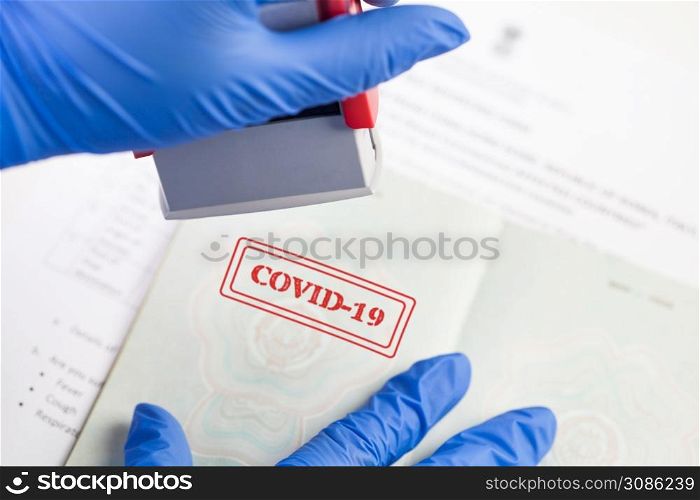 UK border security officer wearing blue protective gloves stamping COVID-19 onto document,health passport or immunity passport,risk free certificate concept,convalescent recovered Coronavirus patient