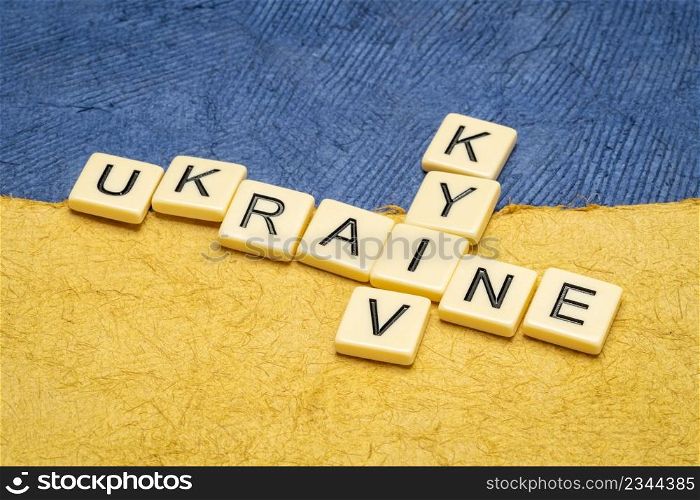 Ukraine and Kyiv crossword in ivory letter tiles against paper abstract in colors of Ukrainian national flag, blue and yellow