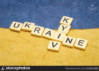 Ukraine and Kyiv crossword in ivory letter tiles against paper abstract in colors of Ukrainian national flag, blue and yellow