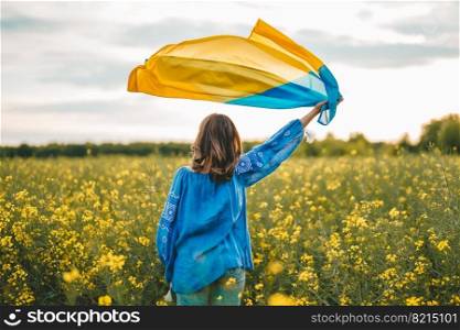 Ukrainian patriot woman waving national flag in canola yellow field. Rare, back view. Ukraine unbreakable, peace, independence, freedom, victory in war. High quality photo. Ukrainian patriot woman waving national flag in canola yellow field. Rare, back view. Ukraine unbreakable, peace, independence, freedom, victory in war.