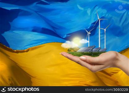 Ukrainian renewable energy - solar panels and wind turbines on green meadow with tree on womans hand against flag of Ukraine on the background. solar panels and wind turbines against flag of Ukraine