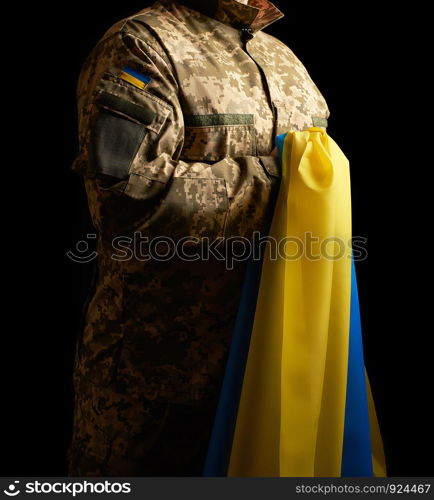 Ukrainian soldier holds in his hand the yellow-blue flag of the state, he pressed his hand to his chest, concept of the memory of the dead soldiers