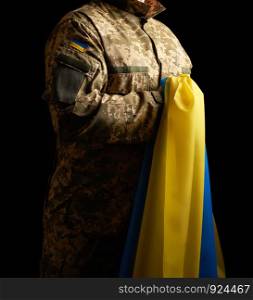 Ukrainian soldier holds in his hand the yellow-blue flag of the state, he pressed his hand to his chest, concept of the memory of the dead soldiers