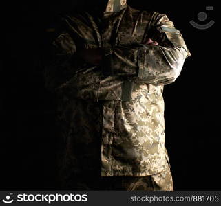 Ukrainian soldier in camouflage uniform stands with arms crossed on his chest, concept of veterans, dark key