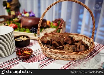 Ukrainian-style table with a basket of bread, peppers and baked pork on a table with Ukrainian tablecloth embroidered. selective focus. Ukrainian-style table with a basket of bread, peppers and baked pork on a table with Ukrainian tablecloth embroidered. selective focus.
