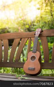 Ukulele on a wooden park bench in summer, green area in the blurry background