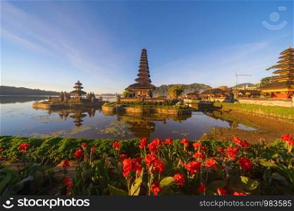 Ulun Danu Bratan Temple, red flowers, and lake in Bali. One of the most popular of tourist attraction. Indonesia. Hindu pargoda architecture of travel trip and holidays vacation in Indonesia.