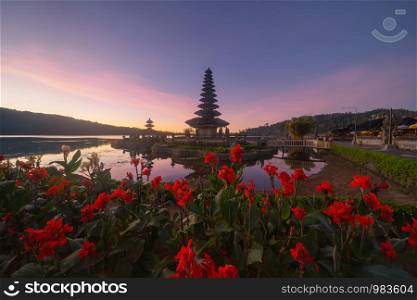 Ulun Danu Bratan Temple, red flowers, and lake in Bali. One of the most popular of tourist attraction. Indonesia. Hindu pargoda architecture of travel trip and holidays vacation in Indonesia.