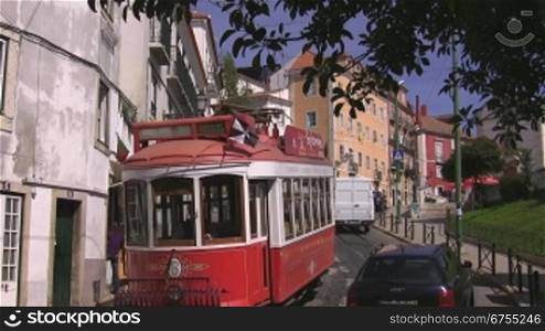 Um die Kurve bergabfahrende rot-wei?e Sightseeing Tram in Lissabon;dahinter und entgegen fahren Autos unnd LieferwSgen.