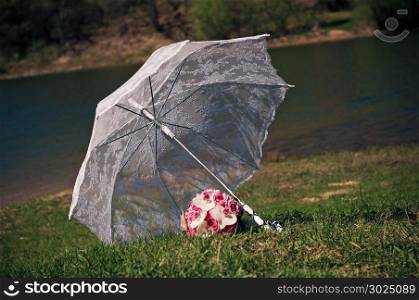 ""Umbrella and bouquet.White transparent umbrella and wedding bouquet on river bank.""