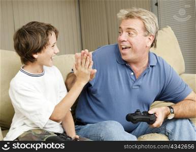 Uncle giving his nephew a high five as they play video games. Could also be father and son.