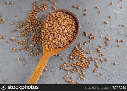 Uncooked brown buckwheat in wooden spoon against grey background. Organic food concept. Buckwheat grains. Ingredients for cooking porridge