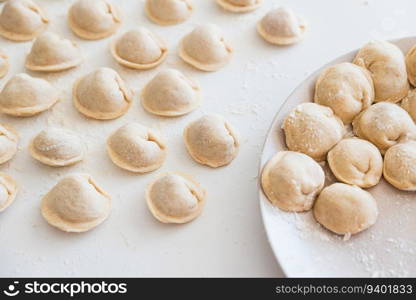 Uncooked homemade pelmeni on white table. Process of making pelmeni, ravioli or dumplings with meat