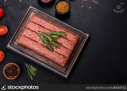 Uncooked Raw beef and lamb meat kebabs sausages on a wooden board. Black background. Fresh raw mince for grilled kebab with spices and herbs on a dark concrete background