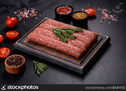 Uncooked Raw beef and lamb meat kebabs sausages on a wooden board. Black background. Fresh raw mince for grilled kebab with spices and herbs on a dark concrete background