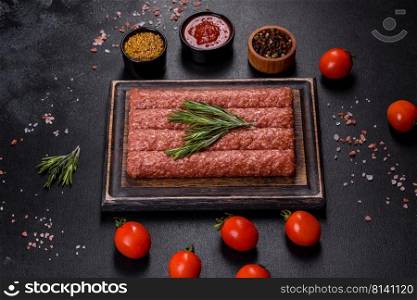 Uncooked Raw beef and lamb meat kebabs sausages on a wooden board. Black background. Fresh raw mince for grilled kebab with spices and herbs on a dark concrete background
