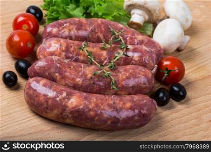 uncooked raw sausages with lettuce, tomatoes, mushrooms on wooden board