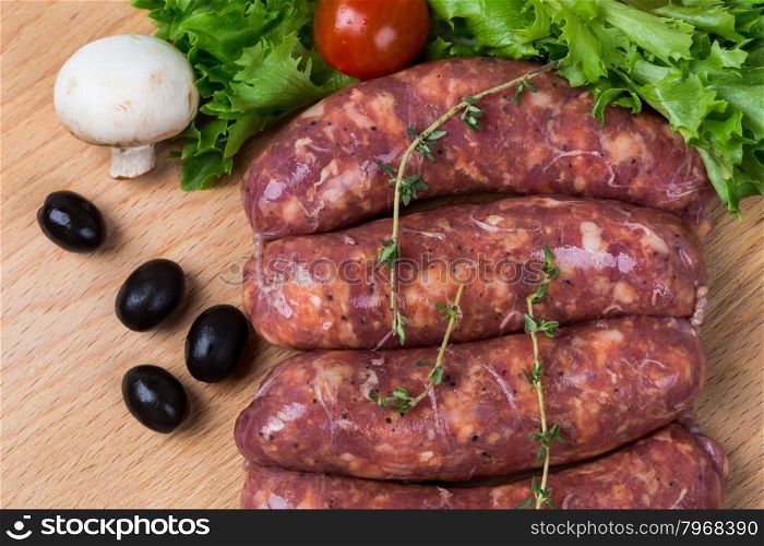 uncooked raw sausages with lettuce, tomatoes, mushrooms on wooden board
