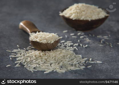Uncooked Rice in a wooden spoon with a wooden bowl in the back ground. 