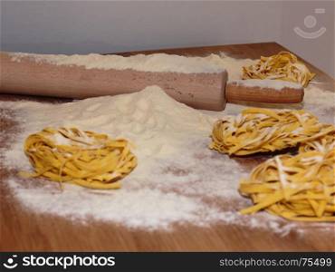 Uncooked Tagliatelle Italian Pasta on Wooden Table with Rolling Pin and Flour