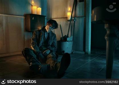 Undead zombie man sitting on lavatory floor. Halloween horror, apocalypse and doomsday concept. Undead zombie man sitting on lavatory floor
