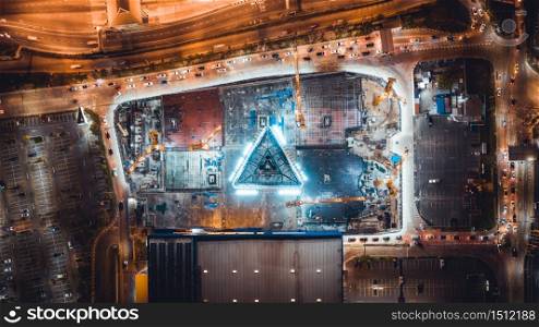 Under construction site, crane, parking lot, and car traffic transportation in Asian city at night. Drone aerial top view. Industrial business or civil engineering technology concept