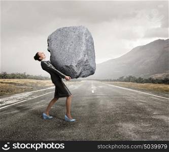 Under pressure of difficulties. Attractive businesswoman carrying big heavy stone